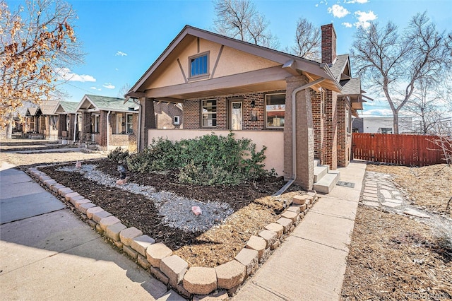 bungalow-style house featuring brick siding, a chimney, fence, and stucco siding