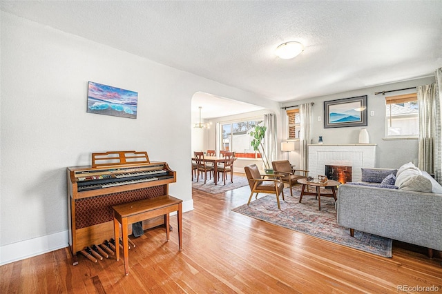 sitting room with a textured ceiling, arched walkways, a fireplace, wood finished floors, and baseboards