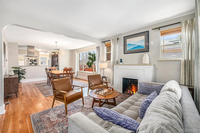 living area with baseboards, a fireplace, a chandelier, and light wood-style floors