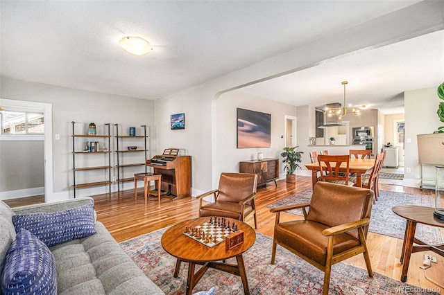 living area featuring a notable chandelier, a textured ceiling, baseboards, and wood finished floors