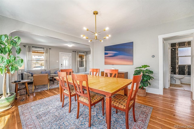 dining area with a chandelier, arched walkways, baseboards, and light wood finished floors