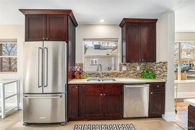 kitchen with appliances with stainless steel finishes, a sink, light countertops, a healthy amount of sunlight, and backsplash