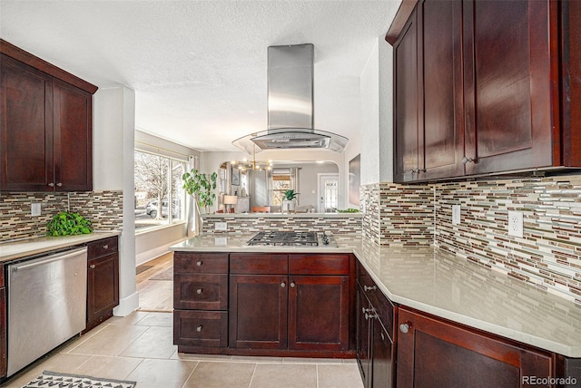 kitchen with appliances with stainless steel finishes, light countertops, decorative backsplash, and island range hood