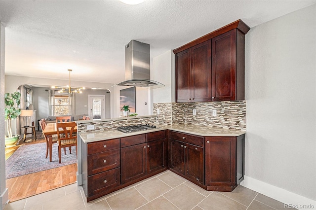 kitchen with range hood, light countertops, stainless steel gas stovetop, decorative backsplash, and a peninsula