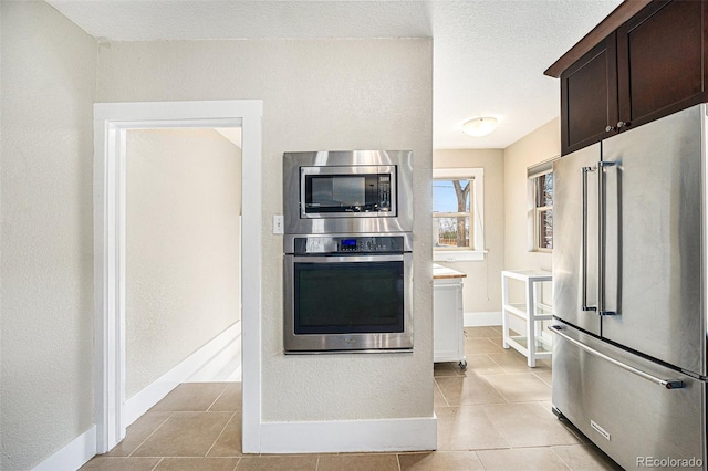 kitchen featuring baseboards, stainless steel appliances, dark brown cabinets, and light tile patterned flooring