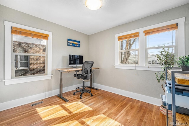 office area with light wood finished floors, visible vents, and baseboards