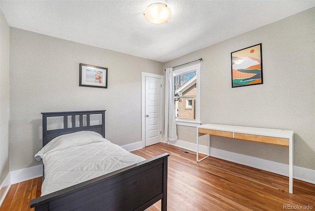 bedroom with visible vents, a textured ceiling, baseboards, and wood finished floors