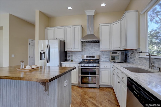 kitchen with a sink, wall chimney range hood, white cabinets, and stainless steel appliances