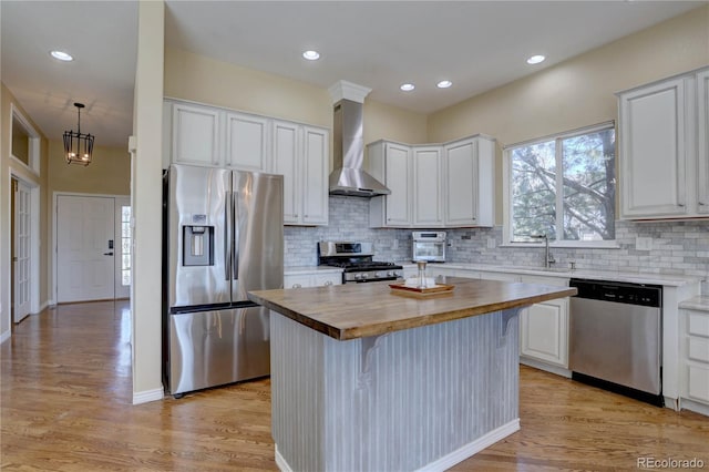 kitchen with wall chimney exhaust hood, a sink, wooden counters, stainless steel appliances, and a kitchen island