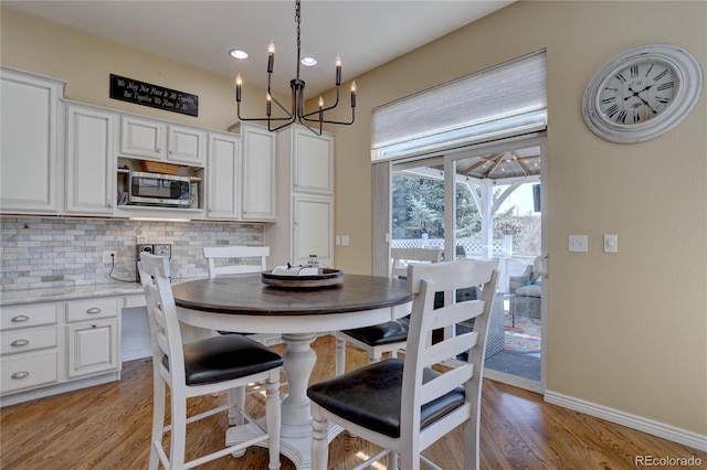 dining space with baseboards, light wood finished floors, and a notable chandelier