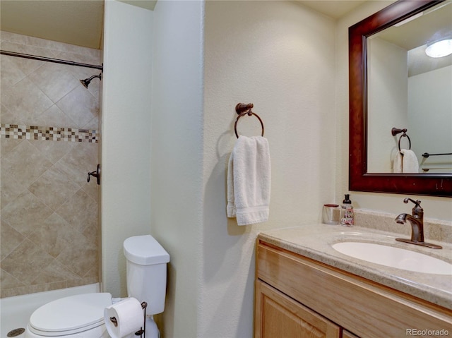 bathroom featuring toilet, tiled shower, and vanity