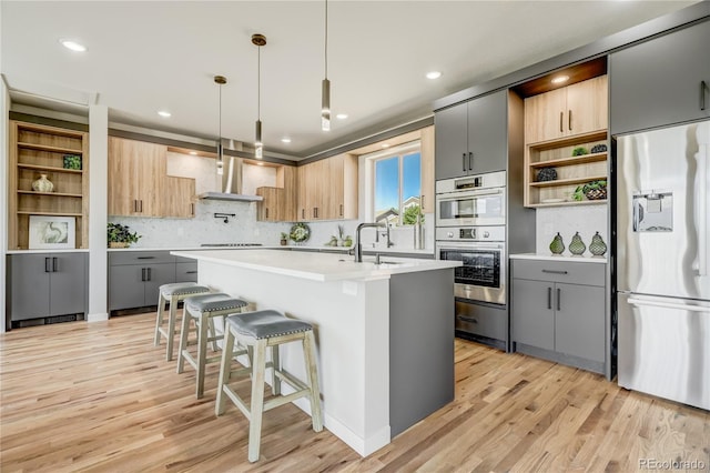 kitchen featuring a kitchen island with sink, stainless steel appliances, gray cabinets, and decorative light fixtures