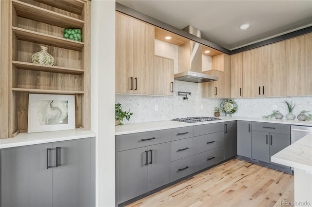 kitchen featuring light hardwood / wood-style floors, tasteful backsplash, wall chimney exhaust hood, and gray cabinetry