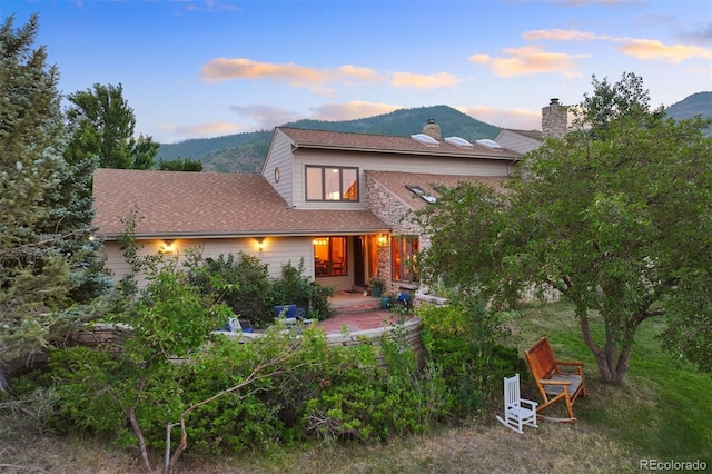 back house at dusk featuring a mountain view and a patio