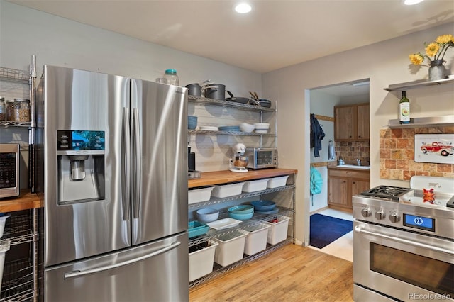 kitchen with light wood-type flooring, appliances with stainless steel finishes, and tasteful backsplash