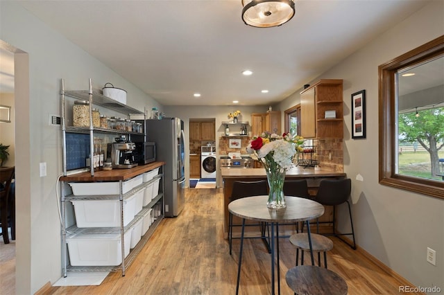 kitchen with wood counters, light hardwood / wood-style flooring, appliances with stainless steel finishes, tasteful backsplash, and washer / clothes dryer