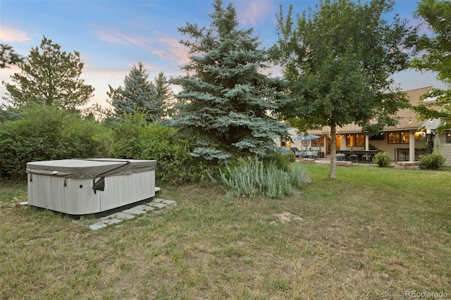 yard at dusk featuring a hot tub and a patio area