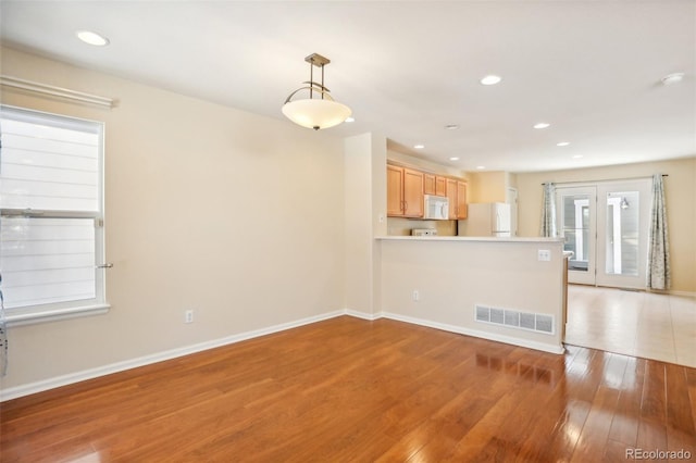 interior space featuring kitchen peninsula, light brown cabinetry, light wood-type flooring, white appliances, and hanging light fixtures