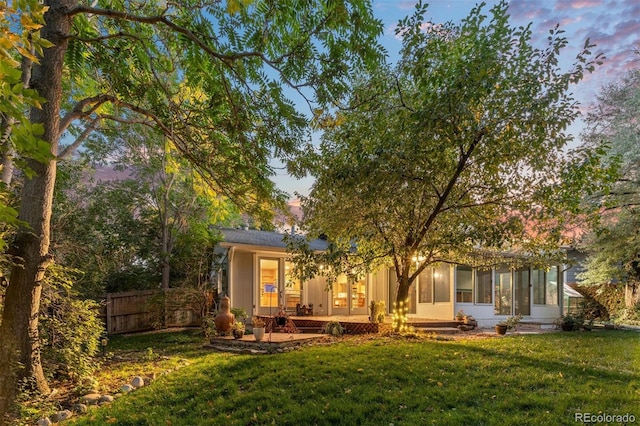 back house at dusk featuring a lawn