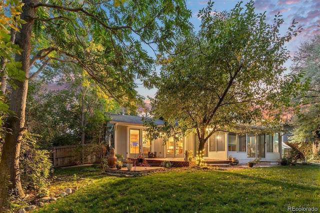 back house at dusk featuring a lawn