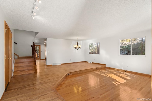 unfurnished living room featuring hardwood / wood-style flooring, a healthy amount of sunlight, a textured ceiling, and a chandelier
