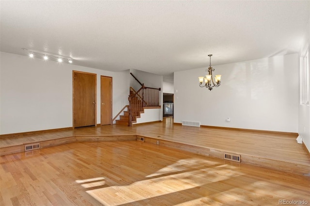 empty room with a notable chandelier, wood-type flooring, and a textured ceiling