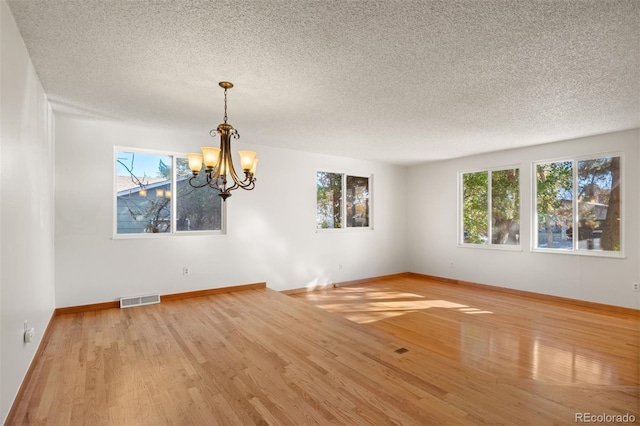 spare room featuring a wealth of natural light, an inviting chandelier, and light wood-type flooring