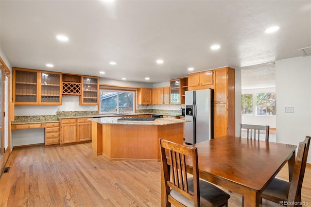 kitchen with sink, light stone counters, light hardwood / wood-style flooring, stainless steel fridge, and a kitchen island