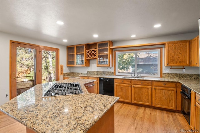 kitchen featuring black appliances, a healthy amount of sunlight, light stone counters, and light hardwood / wood-style floors