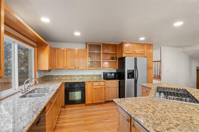 kitchen featuring light stone counters, sink, black appliances, and light hardwood / wood-style flooring