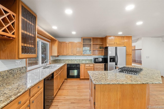kitchen with a center island, black appliances, sink, light stone countertops, and light hardwood / wood-style floors
