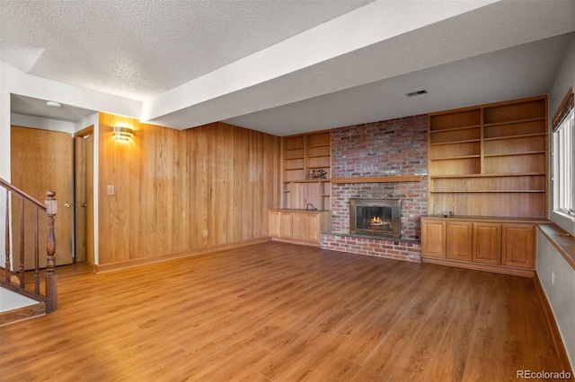 unfurnished living room with a textured ceiling, built in features, a fireplace, light hardwood / wood-style floors, and wood walls