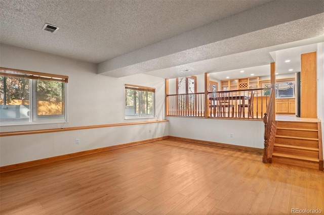 unfurnished room with a healthy amount of sunlight, a textured ceiling, and light wood-type flooring