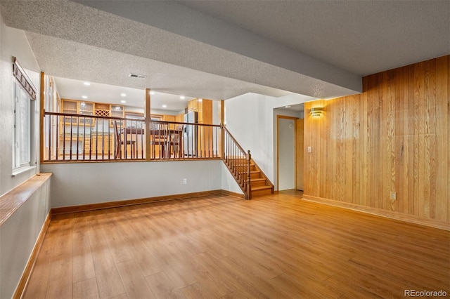 unfurnished room with hardwood / wood-style floors, wood walls, and a textured ceiling