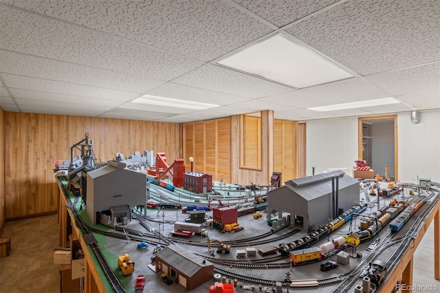 game room with a drop ceiling and wooden walls