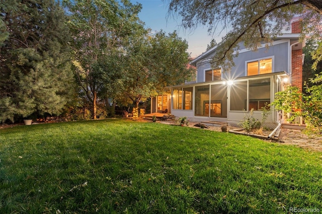 back house at dusk with a lawn and a sunroom