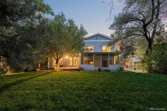 back house at dusk featuring a sunroom, an outdoor structure, and a yard
