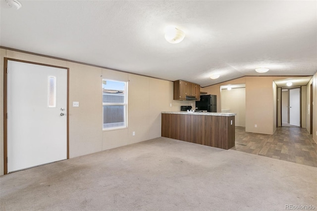 kitchen featuring kitchen peninsula, light carpet, black fridge, and lofted ceiling