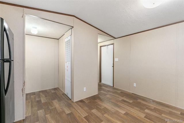 interior space with wood-type flooring, a textured ceiling, vaulted ceiling, and ornamental molding