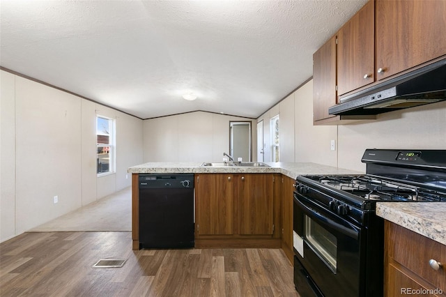 kitchen with kitchen peninsula, a textured ceiling, vaulted ceiling, black appliances, and hardwood / wood-style flooring