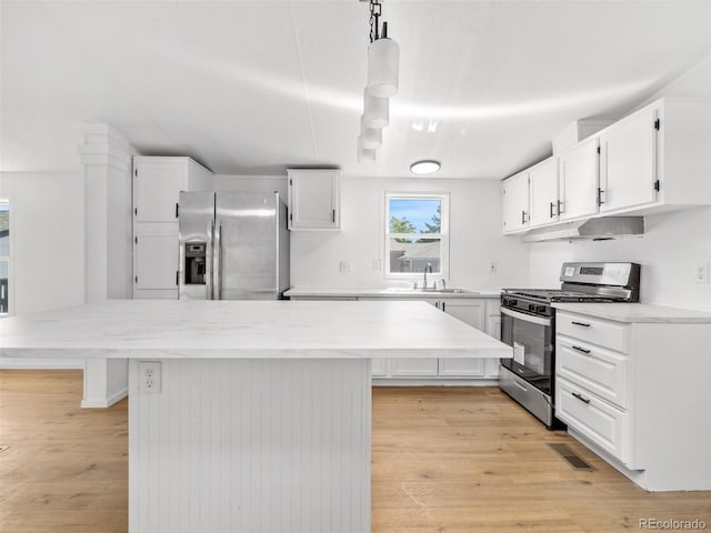 kitchen featuring decorative light fixtures, sink, white cabinetry, light hardwood / wood-style floors, and stainless steel appliances