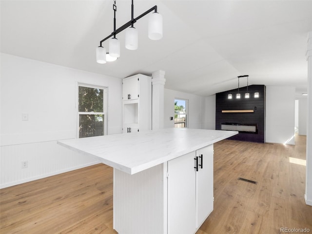 kitchen with pendant lighting, light hardwood / wood-style flooring, vaulted ceiling, white cabinets, and a fireplace