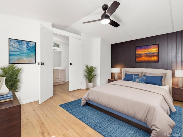 bedroom with light wood-type flooring, ceiling fan, wood walls, and ensuite bath