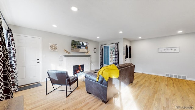 living area featuring a brick fireplace, recessed lighting, visible vents, and light wood finished floors