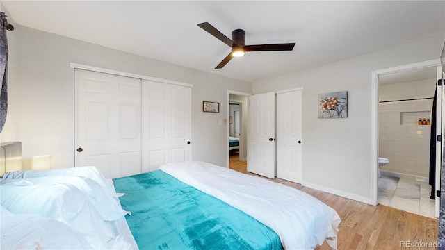 bedroom featuring two closets, ensuite bath, light wood finished floors, baseboards, and ceiling fan