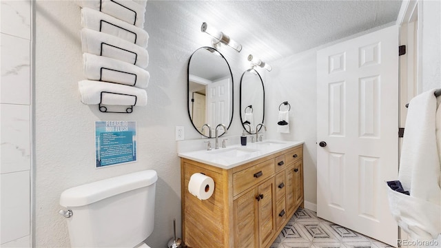 bathroom with a sink, double vanity, toilet, and a textured ceiling