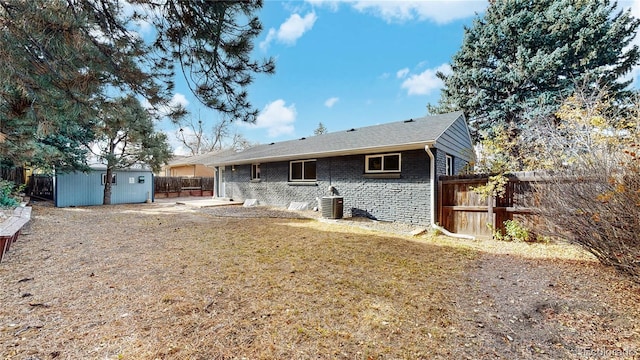 rear view of house featuring central AC unit, a fenced backyard, an outdoor structure, a lawn, and brick siding