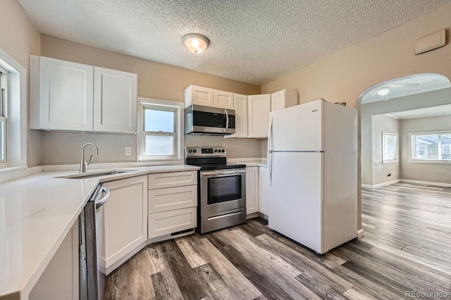 1746 Galena St, Aurora, CO 80010 - kitchen featuring appliances with stainless steel finishes, a sink, wood finished floors, a textured ceiling, and white cabinets