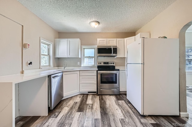 1746 Galena St, Aurora, CO 80010 - kitchen with stainless steel appliances, a sink, a textured ceiling, arched walkways, and dark wood-type flooring