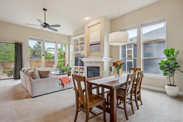 dining area with light carpet, ceiling fan, a tiled fireplace, and baseboards